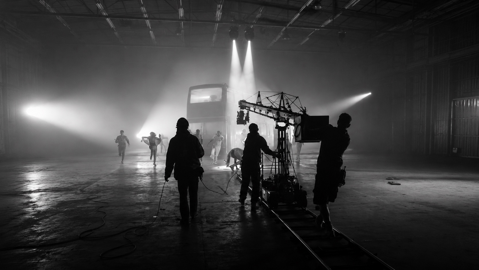 Plateau de tournage en noir et blanc : équipe technique en silhouette autour d'un travelling, projecteurs dans la brume
